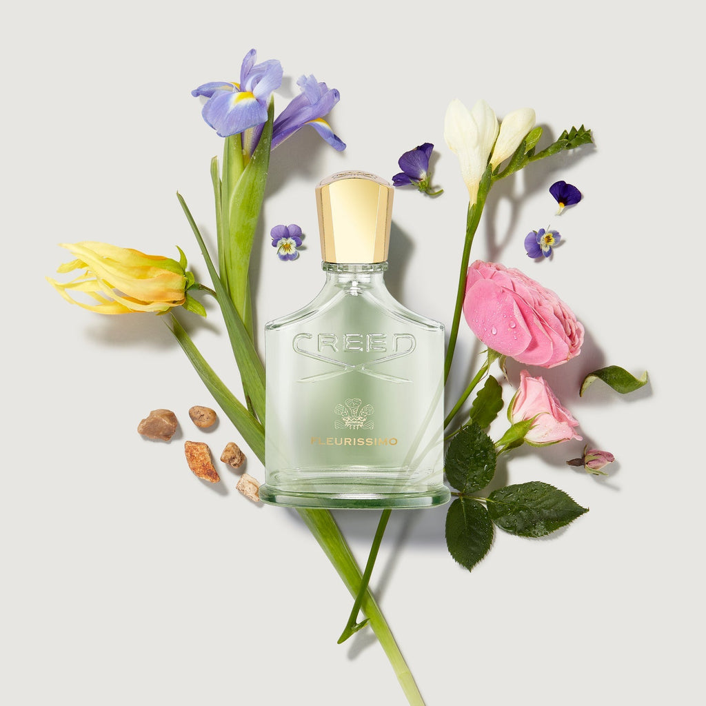 Creed perfume bottle surrounded by flowers on a light background