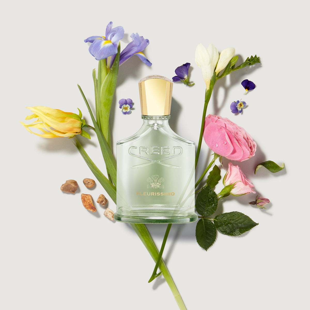 Creed perfume bottle surrounded by flowers on a light background