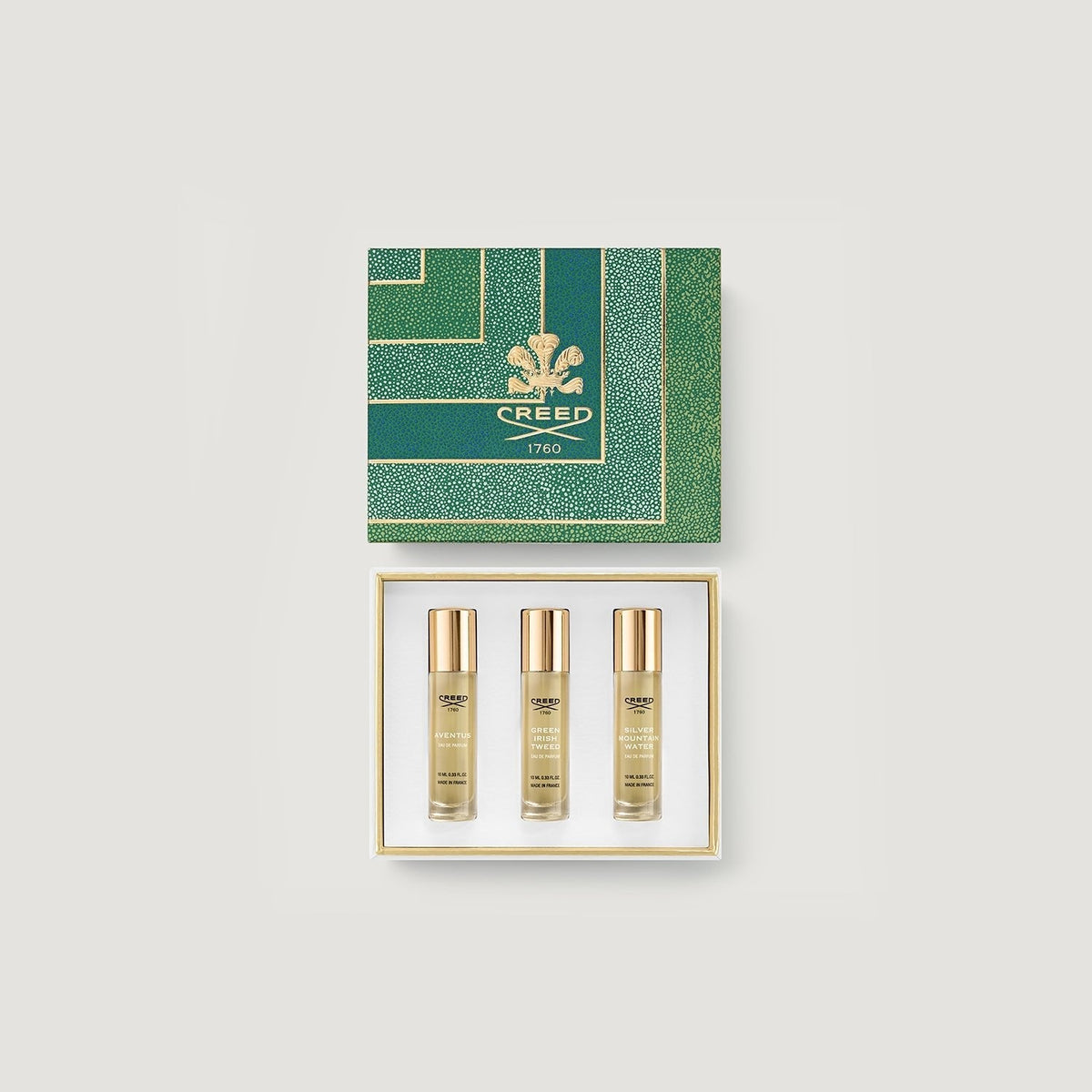Three Creed perfume bottles in a gold and green box on a grey background