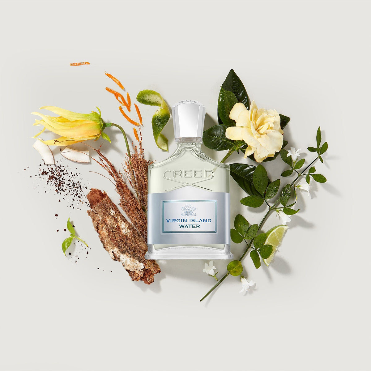 Creed Virgin Island Water perfume bottle surrounded by flowers and leaves on a light background