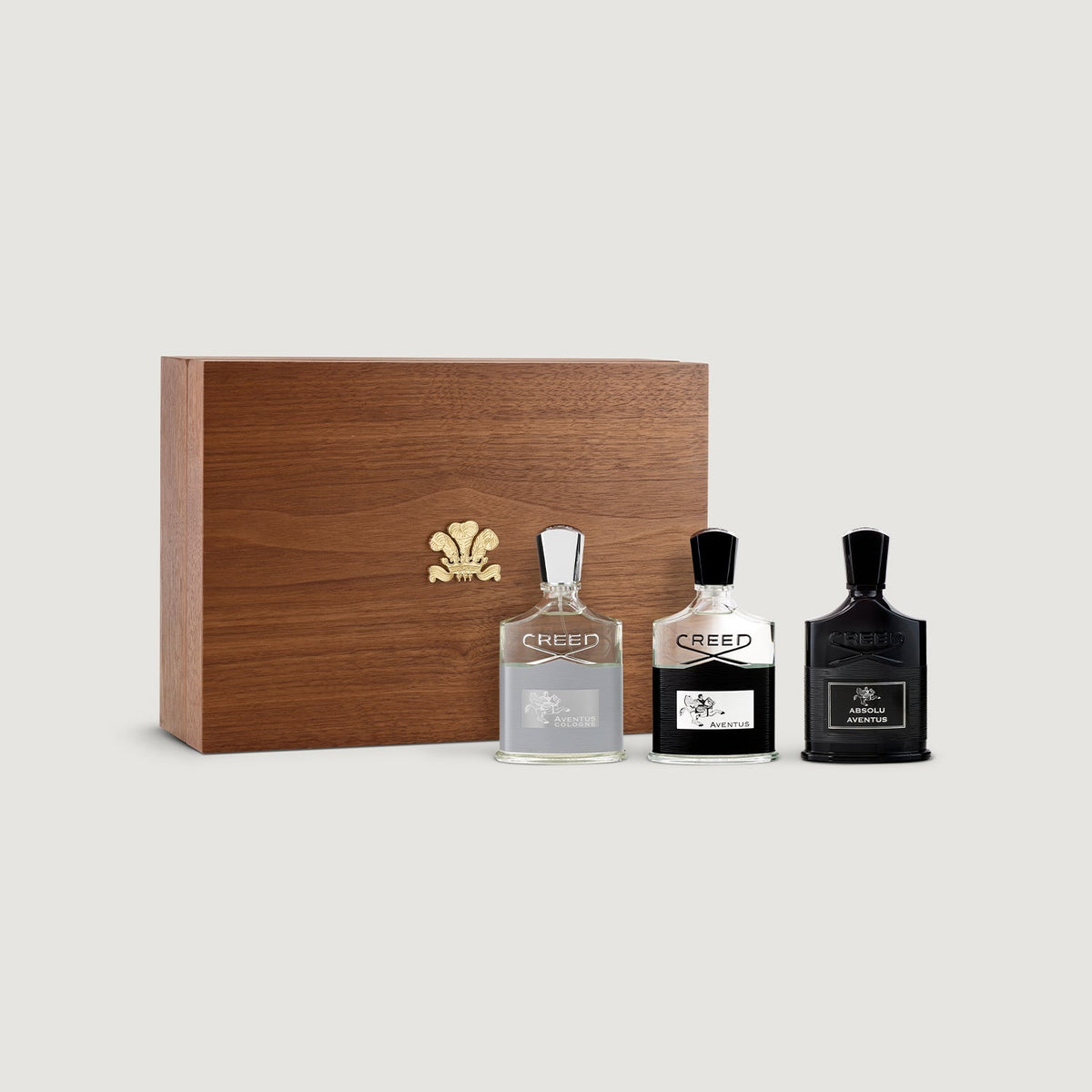 Three Creed perfume bottles with a wooden box on a light gray background