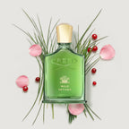 Green Creed Wild Vetiver perfume bottle surrounded by grass, berries, and pink petals on a light gray background