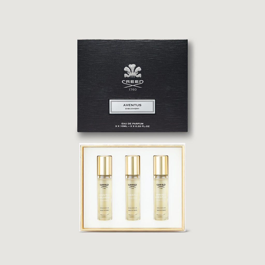Creed Aventus perfume set with three bottles and a black box on a light gray background